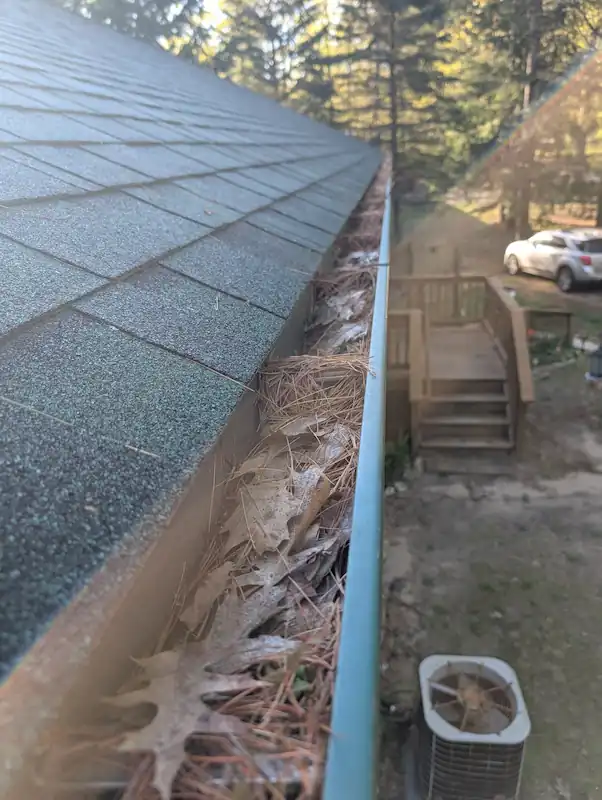 Clogged gutter full of debris before cleaning — seasonal home maintenance in Northern Michigan