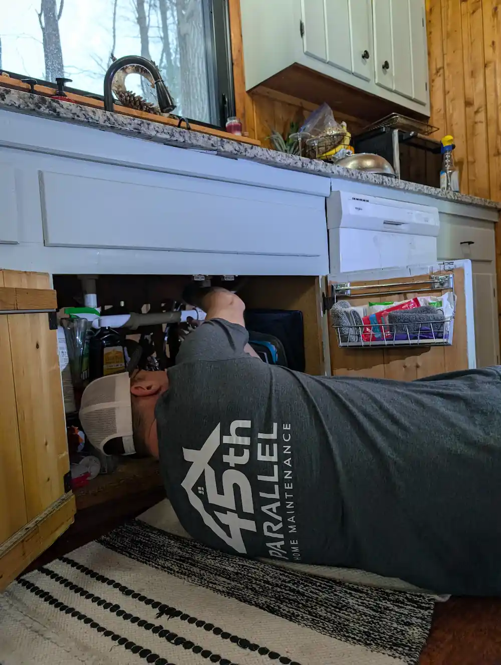 Licensed builder performing plumbing repair under kitchen sink in Traverse City